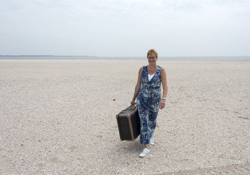 woman with suitcase walking on the beach