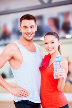 fitness, sport, training, gym and lifestyle concept - smiling woman and man in the gym with water bottle and towel after class