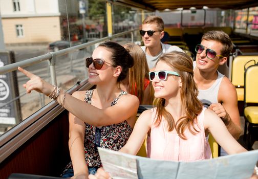 friendship, travel, vacation, summer and people concept - group of smiling friends with map traveling by tour bus