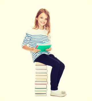 education and school concept - little student girl sitting on stack of books