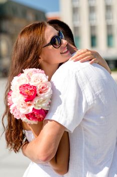 love, wedding, summer, dating and people concept - smiling couple wearing sunglasses with bunch of flowers hugging in city