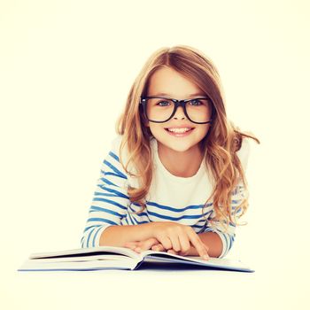 education and school concept - smiling little student girl with book and eyeglasses lying on the floor