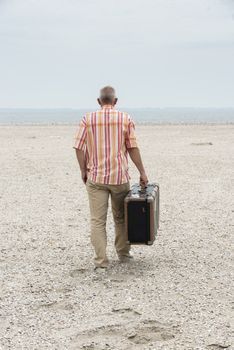 man with old vintage used suitcase walking on the beach