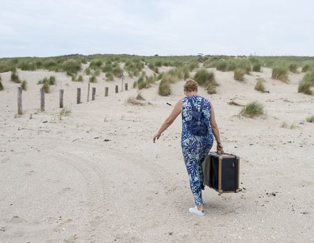 woman with suitcase walking on the beach