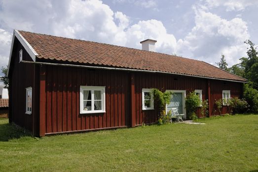 Small red cottage by a green summer meadow.