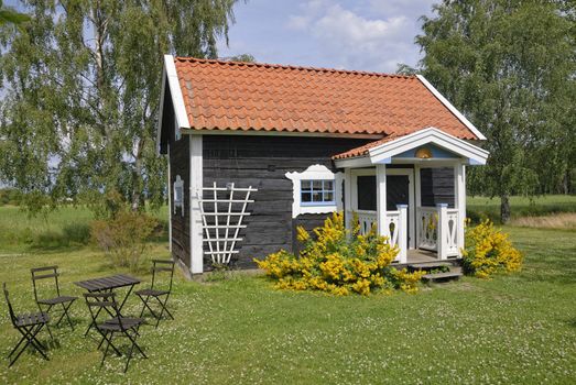 Small brown cottage by a green summer meadow.