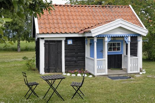 Small brown cottage by a green summer meadow.