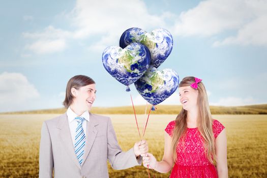 Smiling geeky couple holding red balloons against bright brown landscape