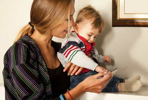 Young beautiful mother and her cute little boy are looking and playing with a smartfone indoors. Copy space frame.