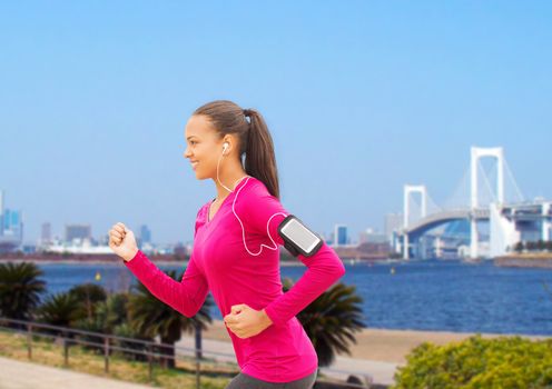 sport, fitness, health, technology and people concept - smiling young african american woman running with smartphone and earphones outdoors