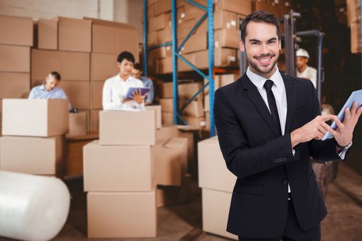 Businessman using his tablet while looking at the camera  against people at work in warehouse