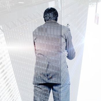 Thinking businessman holding glasses against skyscraper in city