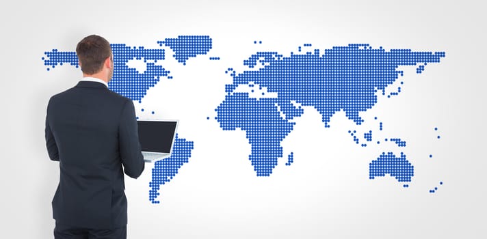 Businessman looking up holding laptop against blue world map