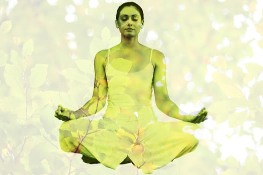 Peaceful woman in white sitting in lotus pose against detail shot of bright green leaves