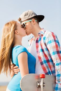 holidays, vacation, love and friendship concept - smiling couple with skateboard kissing outdoors