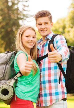 travel, vacation, tourism, gesture and friendship concept - smiling couple with backpacks showing thumbs up in nature