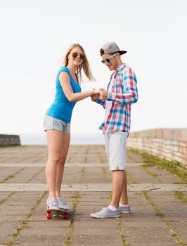 holidays, vacation, love and friendship concept - smiling couple with skateboard riding outdoors