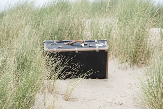 old leather used suitcase hidden in the sandy dunes near the beach