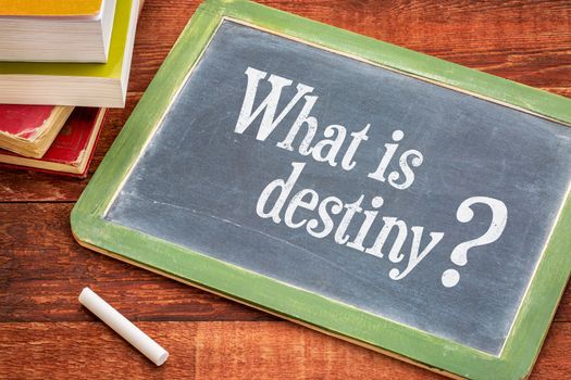 What is destiny question on a slate blackboard with a white chalk and a stack of books against rustic wooden table