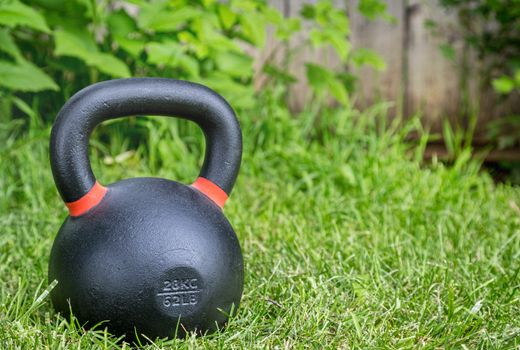 heavy iron competition kettlebell (62lb - 28 kg) on green grass in a backyard - outdoor fitness concept