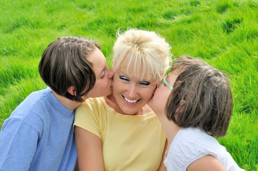 A mother smiles as she receives a kiss on the cheek from her young daughters