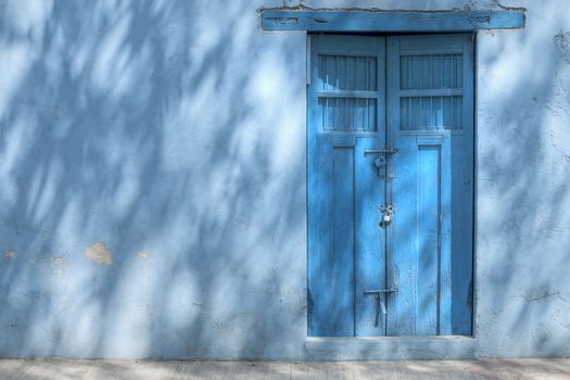 Shadows of three branches filtering sunlight paint the exterior wall and door of a blue building in Valladolid, Mexico