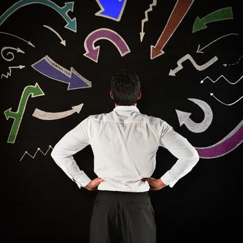 Businessman standing back to the camera with hands on hips against black