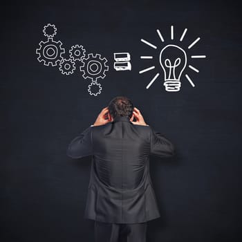Stressed businessman with hands on head against blackboard