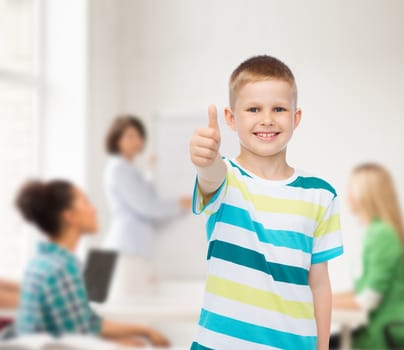 childhood, school, education and people concept - smiling little boy showing thumbs up over group of students in classroom