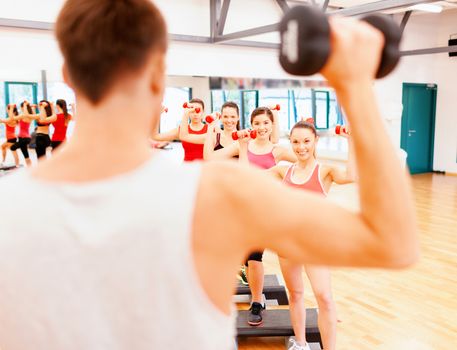 fitness, sport, training, gym and lifestyle concept - group of smiling female with dumbbells and aerobic step an trainer infront