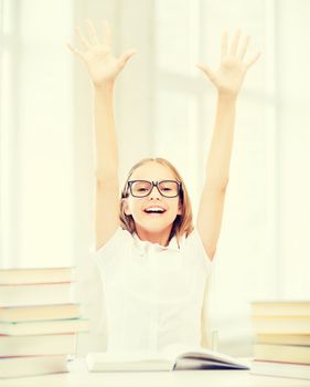 education and school concept - little student girl with books and hands up at school