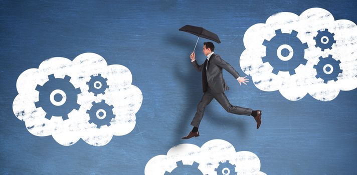 Businessman jumping holding an umbrella against blue chalkboard