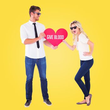 Cool young couple holding red heart against yellow vignette