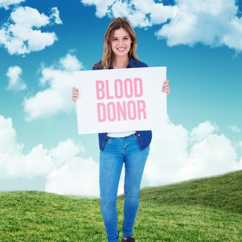 Woman holding poster  against blue sky over green field