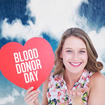 Woman holding heart card and blowing kiss against blue sky