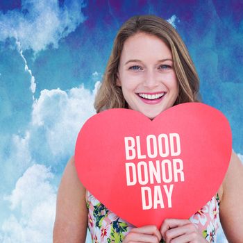 Woman holding heart card  against painted blue sky