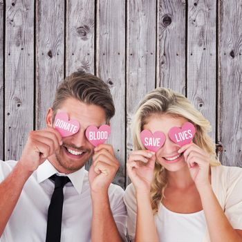 Attractive young couple holding pink hearts over eyes against digitally generated grey wooden planks