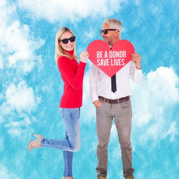 Cool couple holding a red heart together against painted blue sky