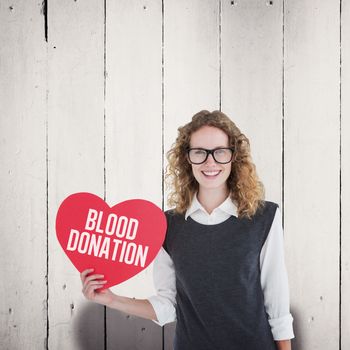 Geeky hipster holding heart card against white wood