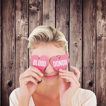 Attractive young blonde holding hearts over eyes against wooden planks background