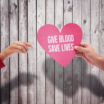 Couple holding a heart against digitally generated grey wooden planks