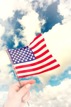 Hand waving american flag against blue sky with white clouds