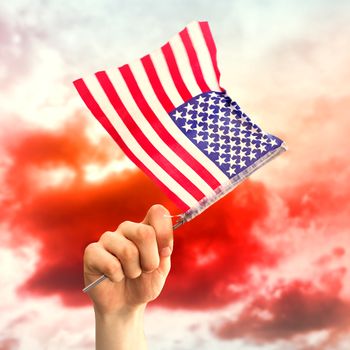 Hand waving american flag against green grass under red cloudy sky