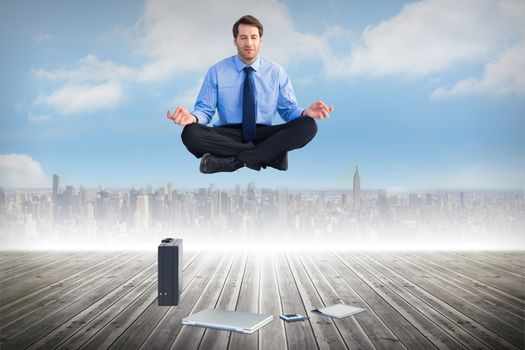 Man sitting in lotus pose with laptop tablet and suitcase against cityscape on the horizon