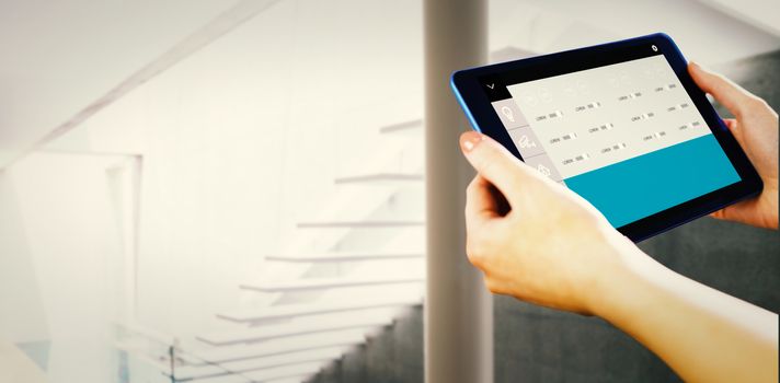 Hands holding tablet against stylish modern home interior with staircase