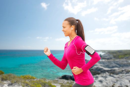 sport, fitness, health, technology and people concept - smiling young african american woman running with smartphone and earphones outdoors