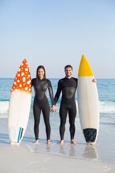 happy couple in wetsuits with surfboard on a sunny day at the beach