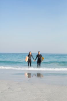 happy couple in wetsuits with surfboard on a sunny day at the beach