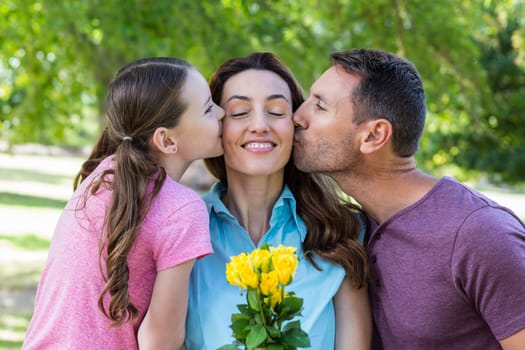 Happy family kissing at camera in the park on a sunny day