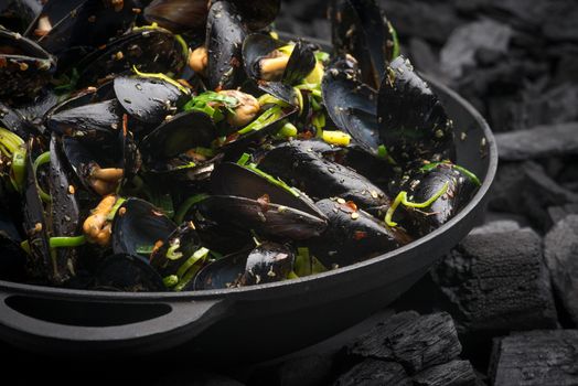 Steamed Mussels with vegetables in a black frying pan on the coals